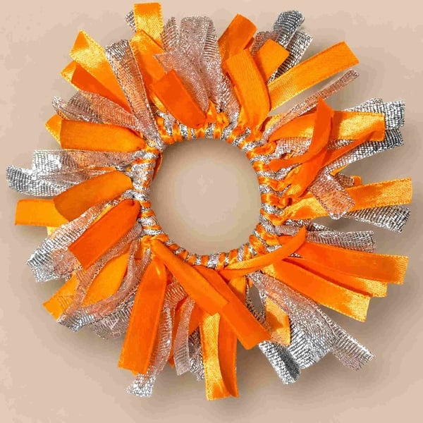 Orange and silver ribbon scrunchie with shimmering metallic strands and bright satin loops, arranged in a full circular design.