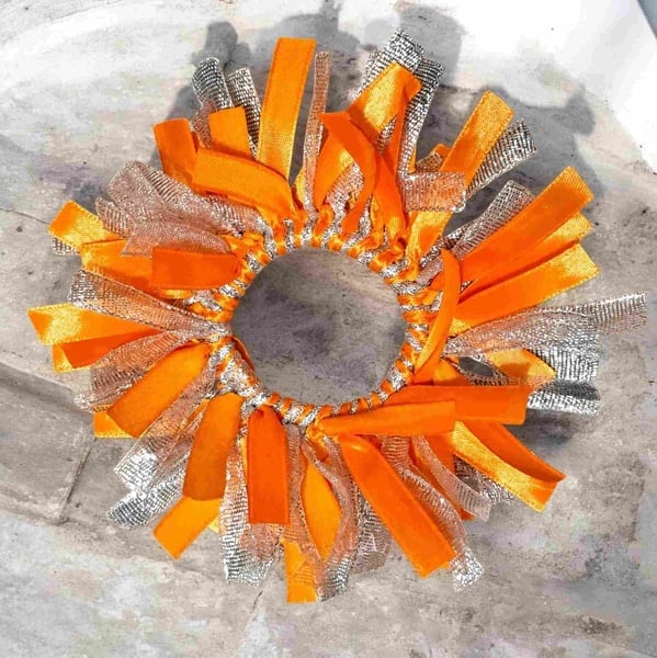 Orange and silver ribbon scrunchie with sparkling metallic strands and satin loops, displayed on a textured stone surface background.