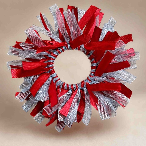 Red and silver ribbon scrunchie featuring layered textured strands and metallic shimmer, displayed on a soft beige background.
