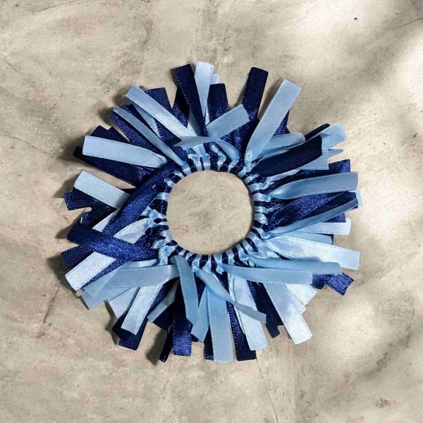 Navy and light blue ribbon scrunchie with layered ribbon streamers on an elastic band, displayed on a stone floor surface outdoors.
