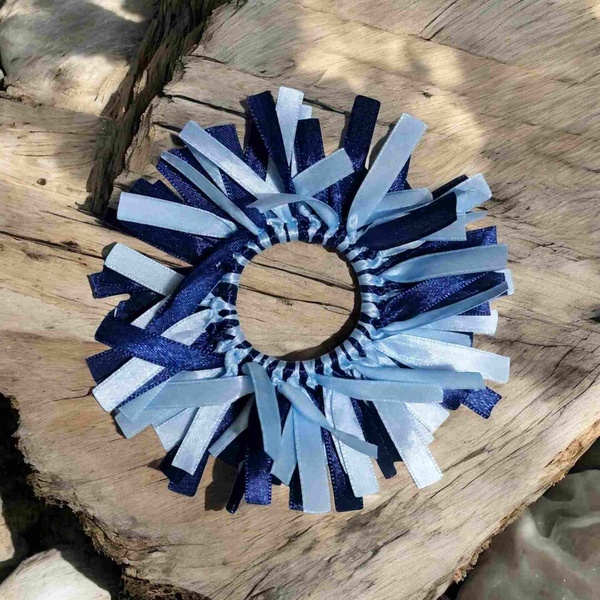 Navy blue and light blue ribbon scrunchie with layered ribbon strips arranged around an elastic band, displayed on natural wood and neutral background
