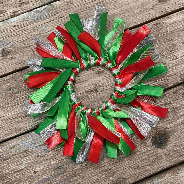 Red, green, and silver ribbon scrunchie arranged in a circle on a rustic weathered wooden deck, featuring festive layered ribbons.