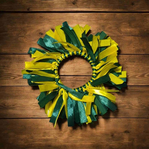 Handmade green and yellow ribbon scrunchie with layered satin and grosgrain streamers displayed on a warm rustic wooden surface.
