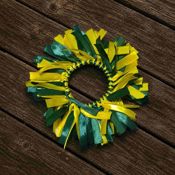 Green and yellow ribbon scrunchie with layered satin and grosgrain streamers arranged in a circle on a rustic weathered wooden deck.
