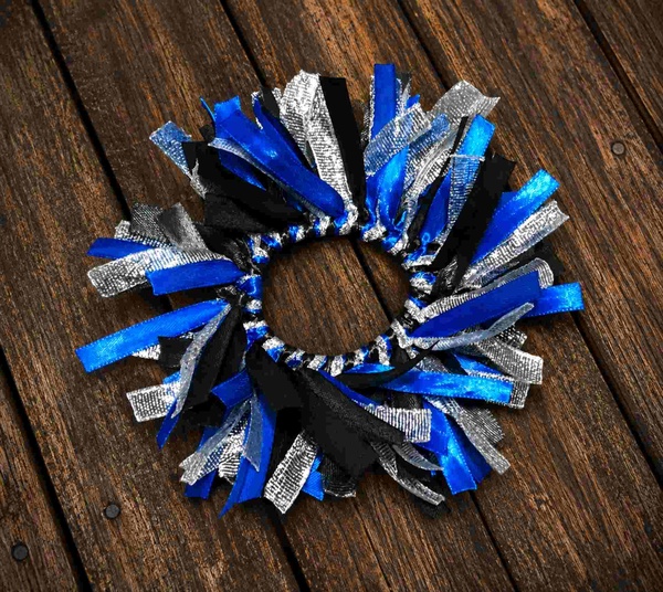 Blue, black, and silver ribbon scrunchie with layered textured ribbons arranged in a full, fluffy design on a rustic dark wooden deck background.