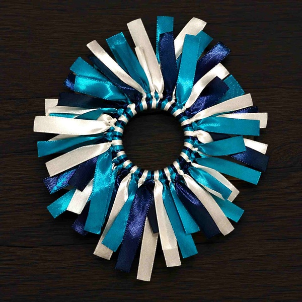 Turquoise, navy and white ribbon scrunchie with layered satin streamers arranged in a full circle on a dark wood surface.