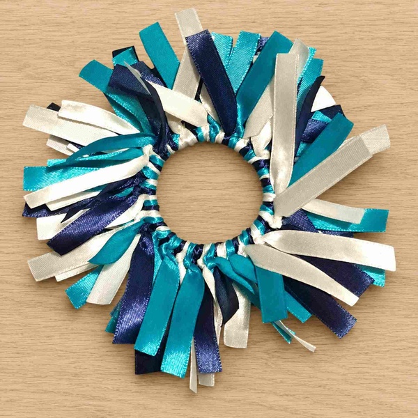 Turquoise navy blue and white ribbon scrunchie with layered satin streamers displayed in a circle on a light oak wood background.
