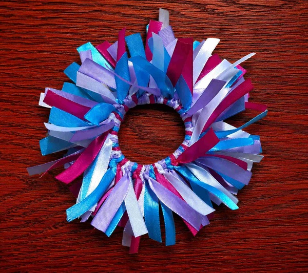 Colorful handmade ribbon scrunchie with blue, pink, white and lavender streamers on a rich red wood background, top view.