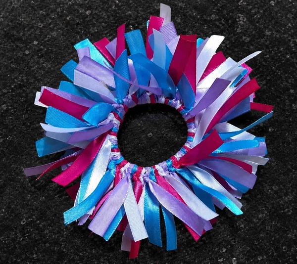 Handmade ribbon scrunchie with bright blue, pink, white and lavender streamers arranged around an elastic ring on dark granite.