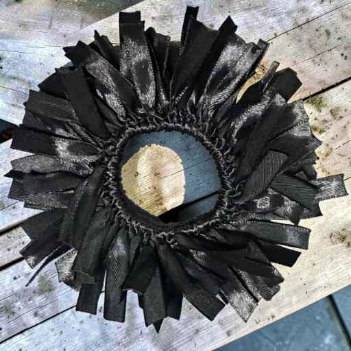 Black circular brush ring with frayed strips radiating outward around a center opening, resting on a weathered wooden surface.