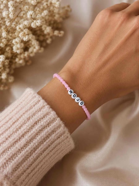 Pink beaded WDJD bracelet on a woman's wrist, styled with a soft knit sweater and neutral floral background, faith jewelry.