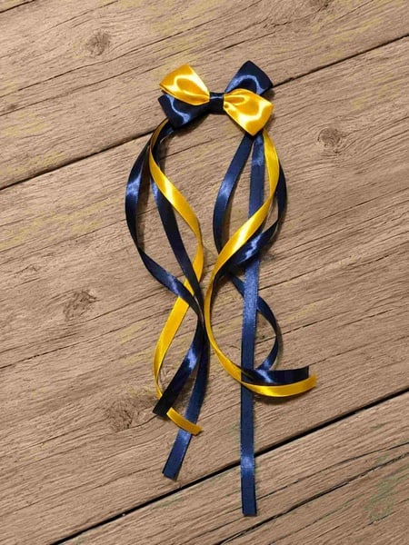 Navy and yellow satin streamer hair bow with long curled ribbon tails displayed on a rustic wooden deck background, handmade accessory.