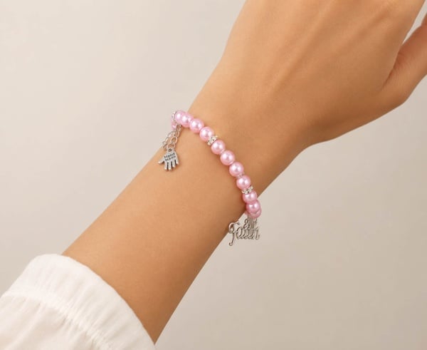 Handmade pink glass bead bracelet with silver Faith charm, crystal spacers and adjustable clasp worn on wrist with neutral background.