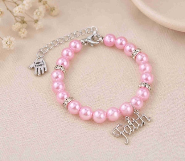 Handmade pink glass pearl bracelet with Faith charm, silver accents and adjustable clasp on a soft neutral background, gift.
