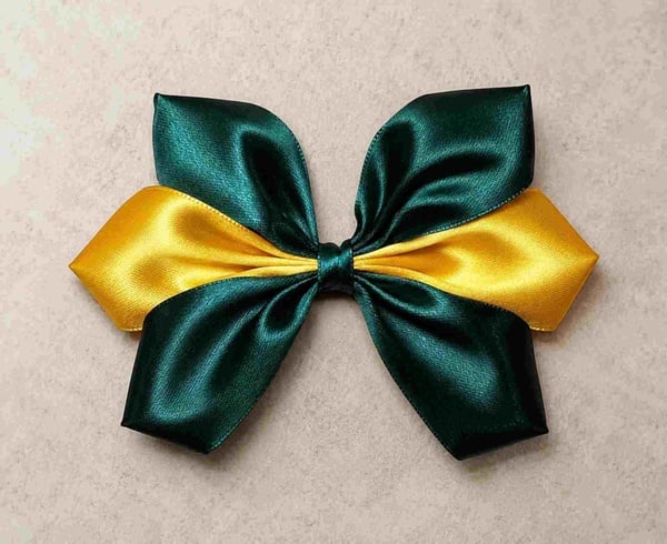 Green and yellow satin layered hair bow with elegant ribbon loops on a neutral background, handmade accessory for girls, schools and teams.