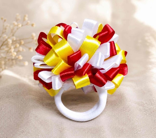 Red, white and yellow handmade ribbon pom pom hair elastic on a neutral linen background, perfect for school, sports and everyday wear.