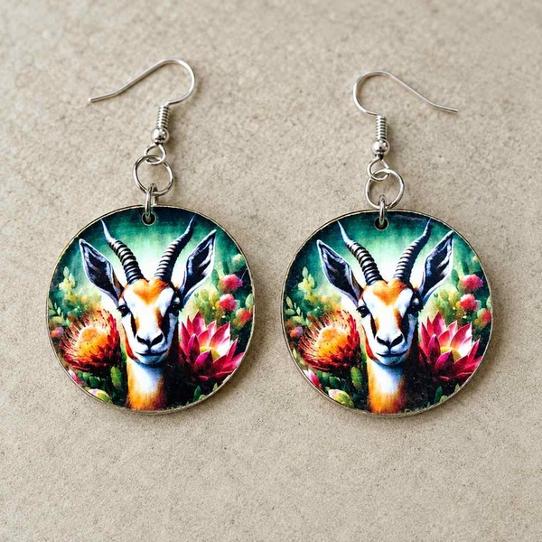 Handmade South African springbok and protea round dangle earrings with hypoallergenic hooks displayed on a neutral stone background.