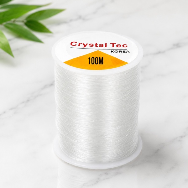 Crystal Tec Korea 100m clear elastic beading cord spool on a clean marble background for jewellery making, crafts and DIY projects.