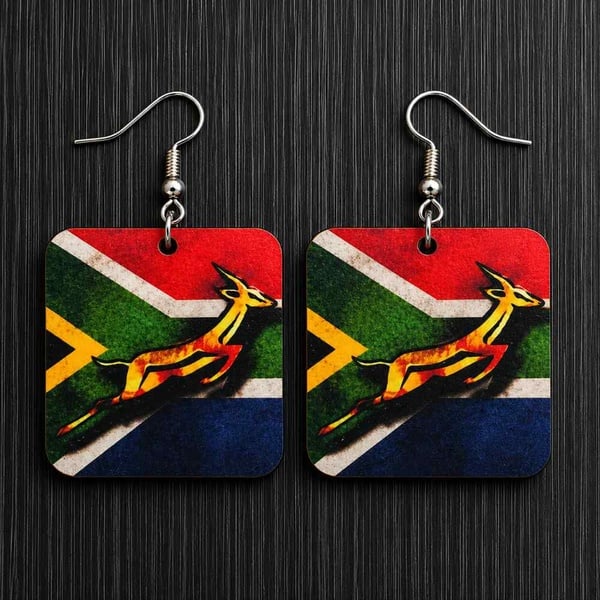 Handmade South African flag springbok dangle earrings on silver hooks displayed on black wood background, lightweight patriotic jewelry.