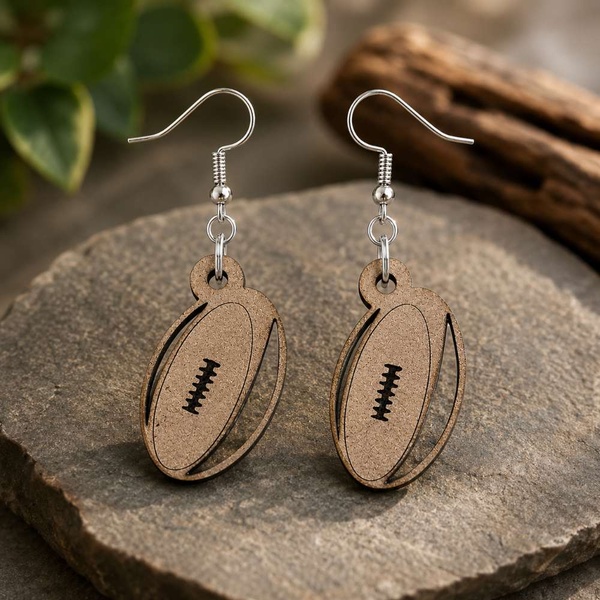 Wooden rugby ball dangle earrings with silver hooks displayed on natural stone, handcrafted sports-inspired jewelry for rugby fans.