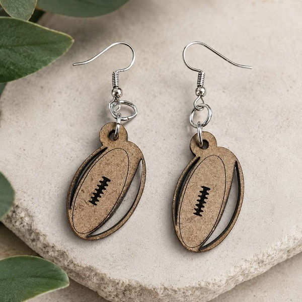 Handmade wooden rugby ball drop earrings with silver hooks on a neutral stone background, lightweight sports fan jewelry gift.