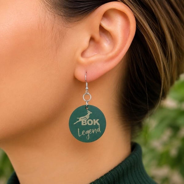Close-up of handmade green BOK Legend Springbok rugby fan earrings worn in a woman's ear with silver hooks in a lifestyle setting.