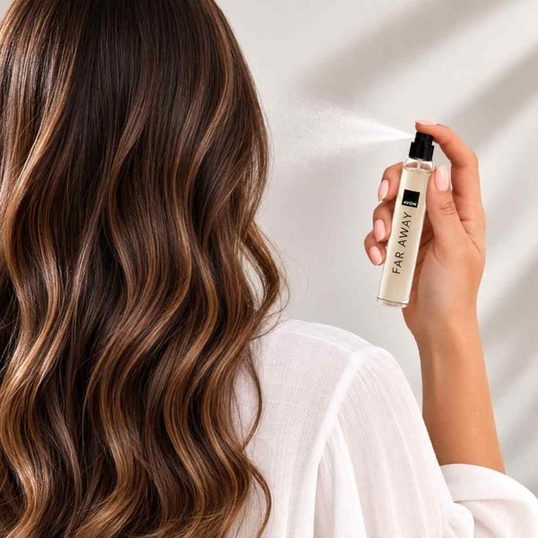 Woman spraying Avon Far Away perfume from behind in a clean lifestyle setting, showcasing a long-lasting floral oriental fragrance.