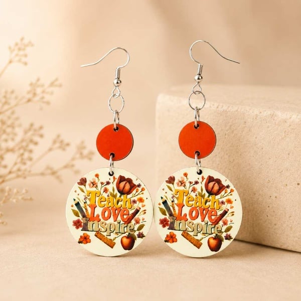 Handmade Teach Love Inspire teacher dangle earrings with orange accents on a neutral beige display, ideal teacher gift.
