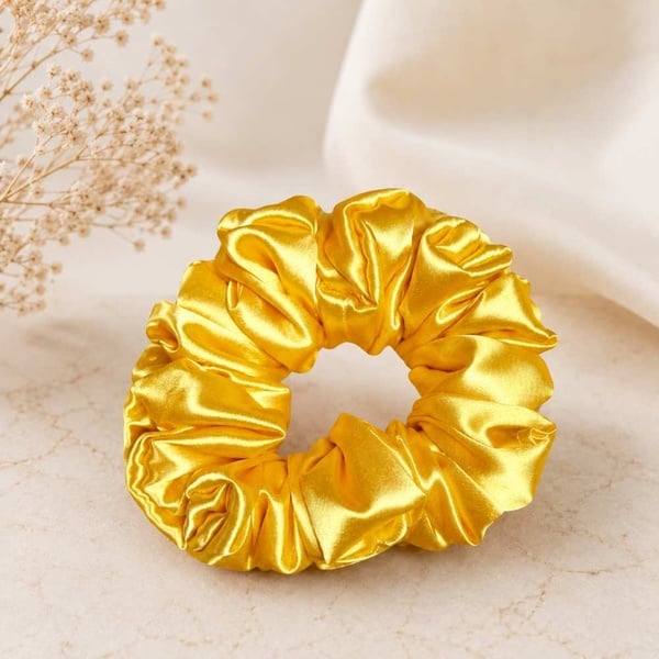Yellow satin hair scrunchie on a soft neutral beige background, beautifully showcased to highlight its silky finish and elegant style.