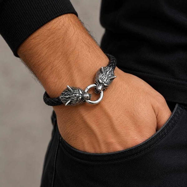 Men's black braided leather bracelet with detailed stainless steel wolf head clasp worn on wrist in premium lifestyle setting.