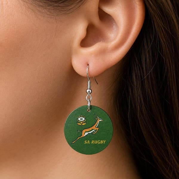 Close-up of handmade SA Rugby Springbok round drop earring with silver hook worn on a woman's ear, lightweight fan jewellery.