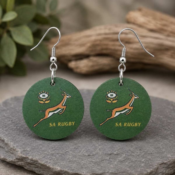 Handmade green SA Rugby round dangle earrings with silver hooks displayed on a natural stone surface with a soft rustic background.