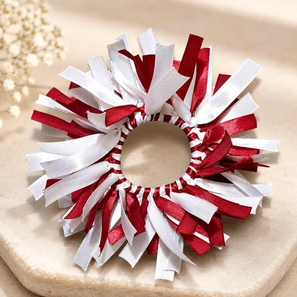 Maroon and white handmade ribbon scrunchie showcased on a soft neutral stone background, highlighting satin texture and festive design.