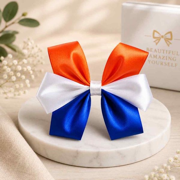 Orange, white and blue satin hair bow showcased on a marble display with a soft neutral e-commerce background for premium product appeal.