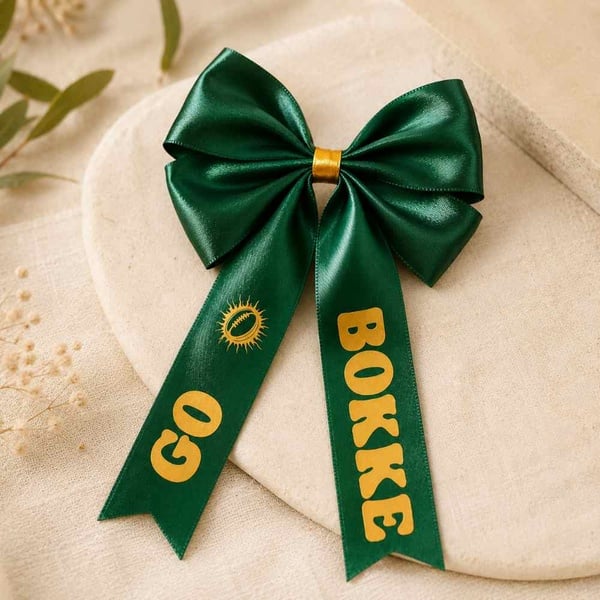 Emerald green satin Go Bokke hair bow with gold print, elegantly displayed on a warm neutral linen background for premium online shopping.