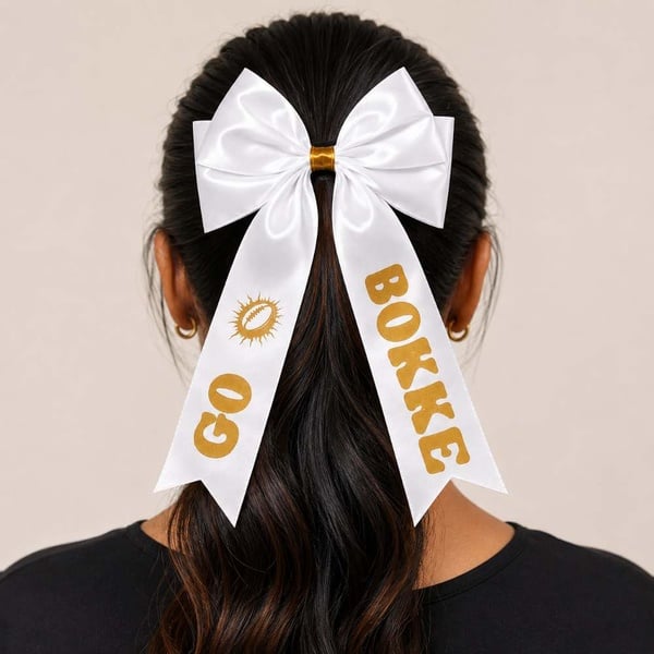 Handmade GO BOKKE white satin supporter hair bow with gold print in an Indian woman's ponytail, viewed from behind.