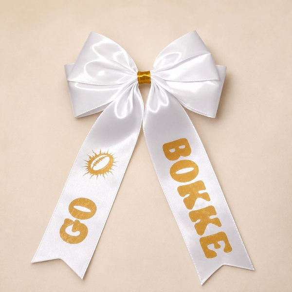 White satin Springbok supporter hair bow with gold center wrap, GO BOKKE print and rugby ball graphic on a soft beige background.