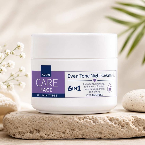 Avon Care Face Even Tone Night Cream 6-in-1 in a white jar on a natural stone display with soft floral background for skincare use.